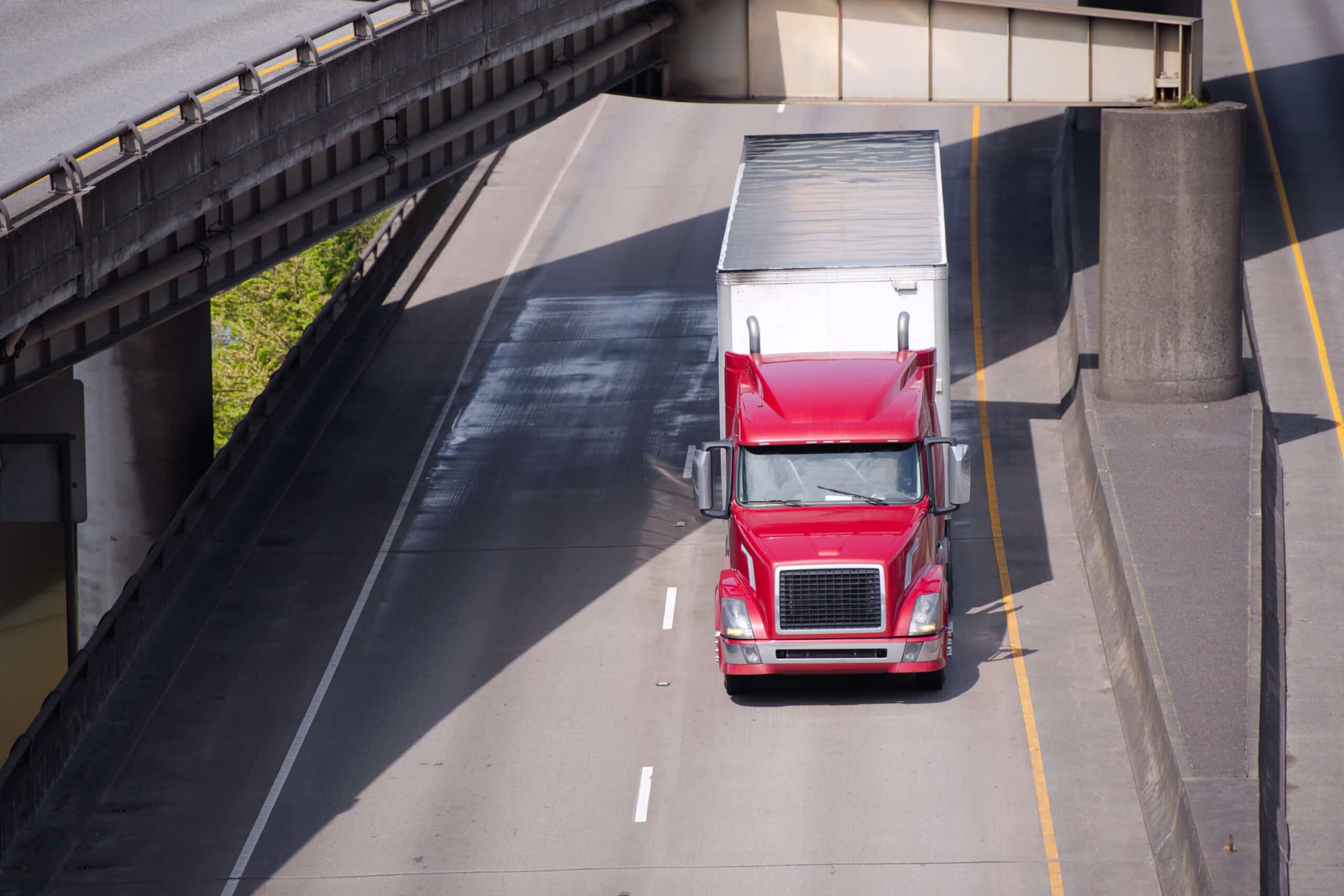 Red modern big rig semi truck with semi trailer going on the road under overpass intersection